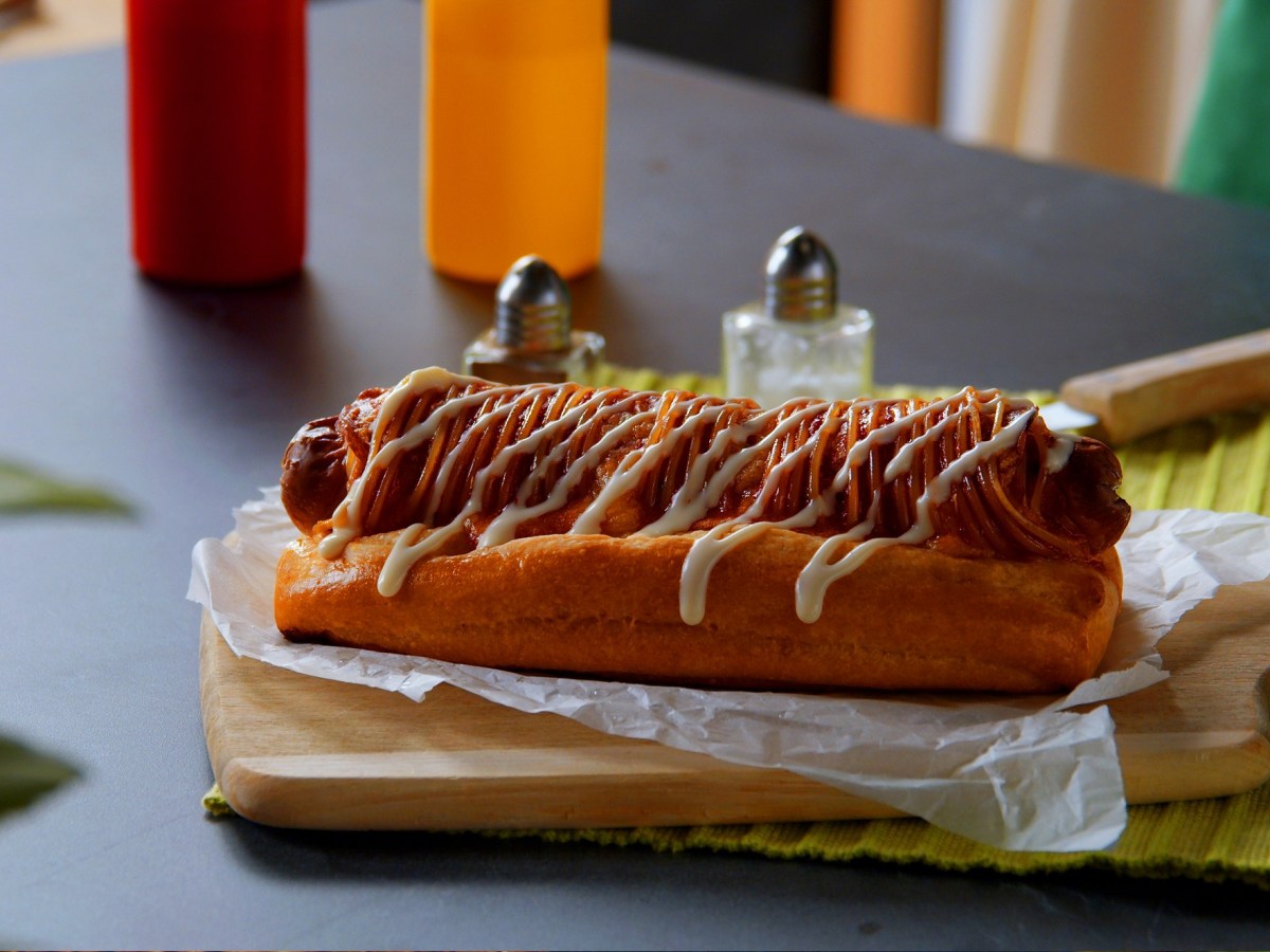 Pizza-Hot-Dog mit Mayonnaise auf einem Brett.