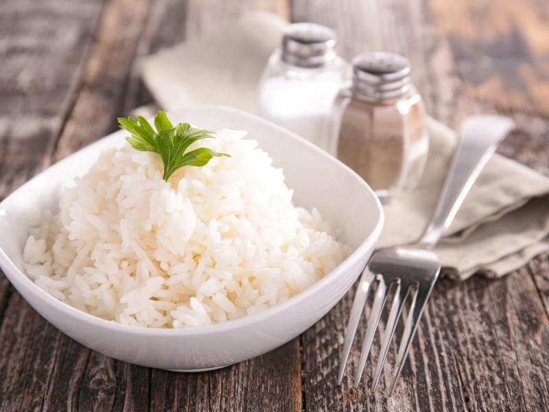 Ist Reis gesund? Eine weiße Schale Reis, daneben eine Gabel, dahinter ein Salz- und ein Pfefferstreuer.