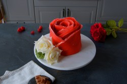 Pfannkuchen-Rose auf einem weißen Teller. Daneben liegen echte Rosen und Himbeeren