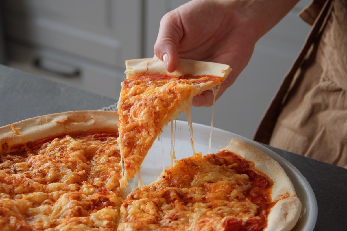 Pizzateig ohne Hefe: Jemand nimmt ein Stück Pizza hoch.