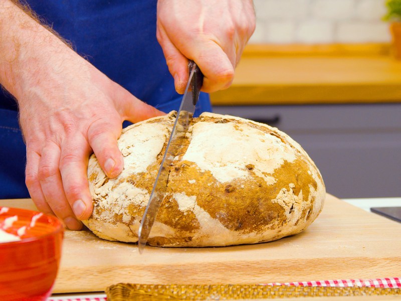 Sauerteigbrot backen: jemand schneidet ein Sauerteigbrot mit dem Messer durch.