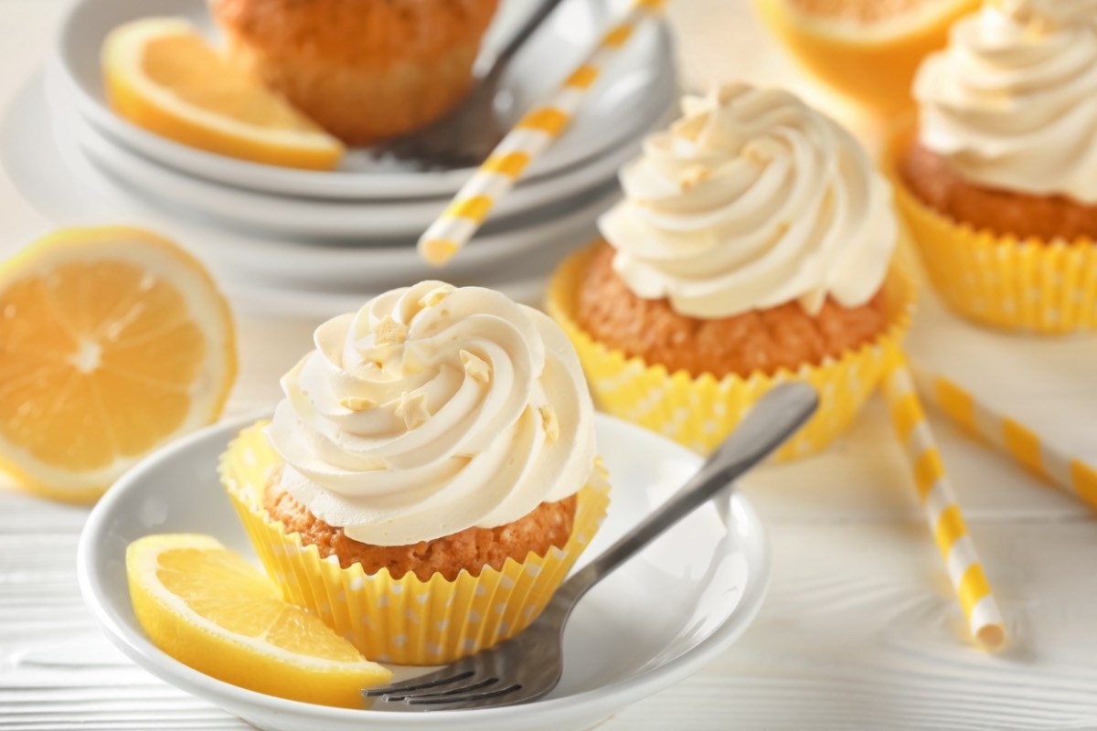 Mehrere Zitronen-Cupcakes mit frischen Zitronenscheiben daneben.