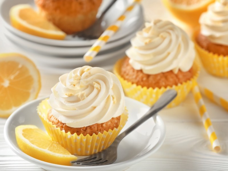 Mehrere Zitronen-Cupcakes mit frischen Zitronenscheiben daneben.