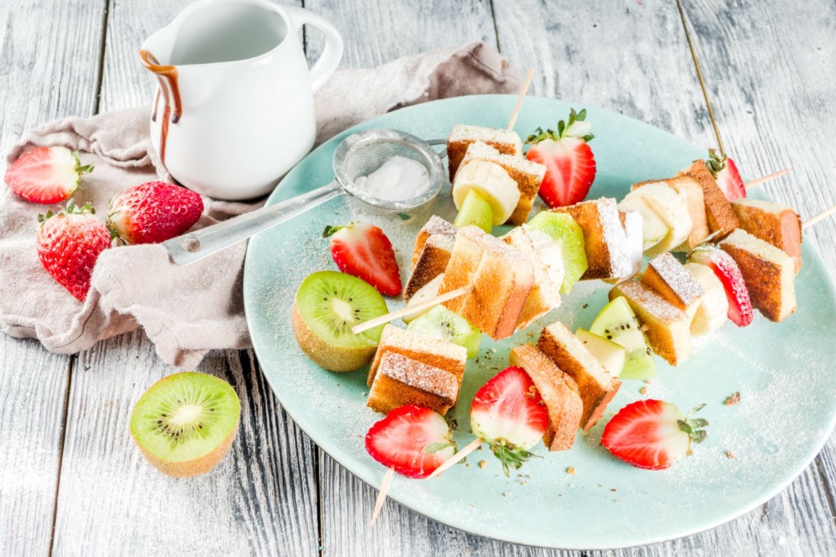 Mehrere French Toasts am Spieß mit Erdbeeren und Kiwis auf einem Teller.