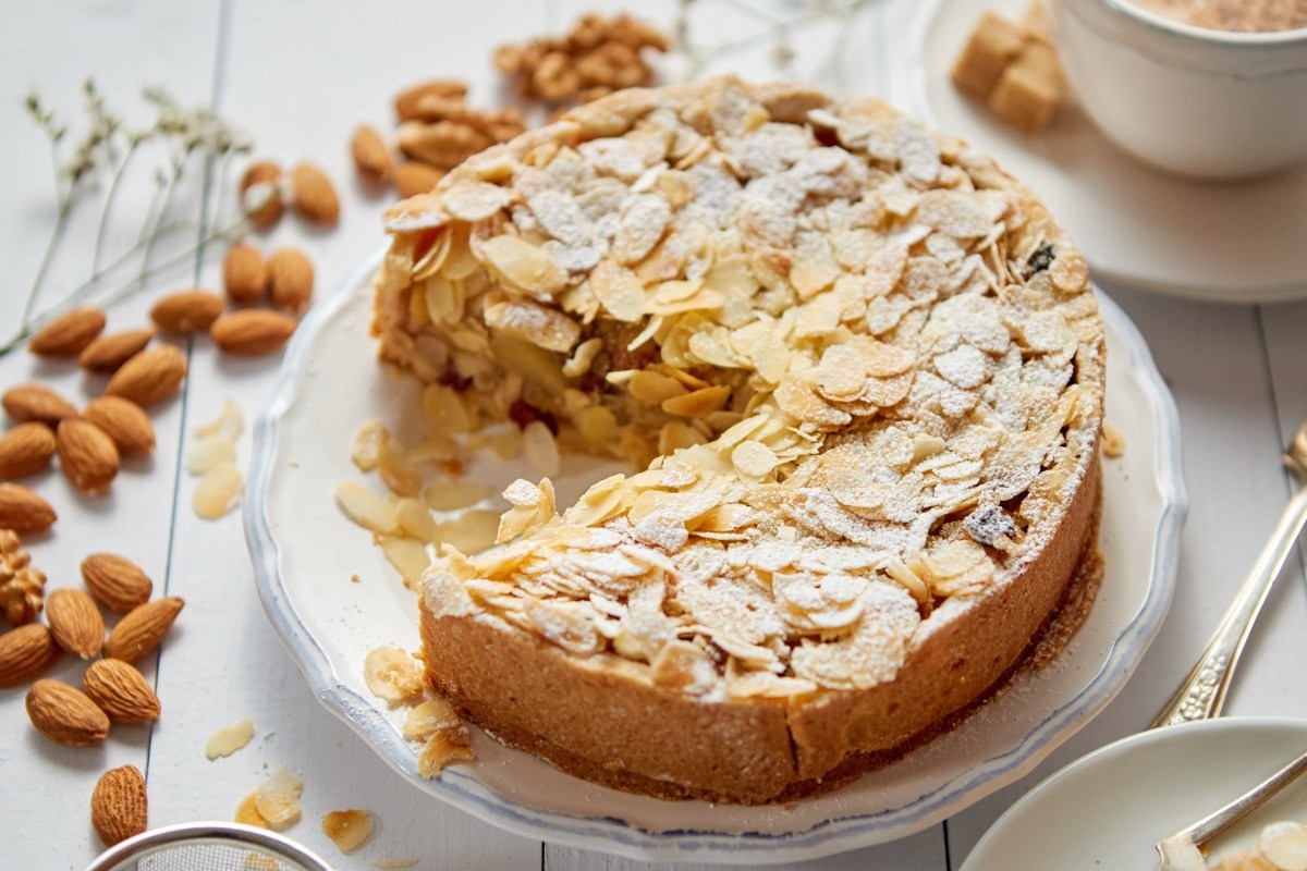 Ein Wiener Apfelkuchen in der Draufsicht. Drumherum liegen Zutaten wie Mandeln.