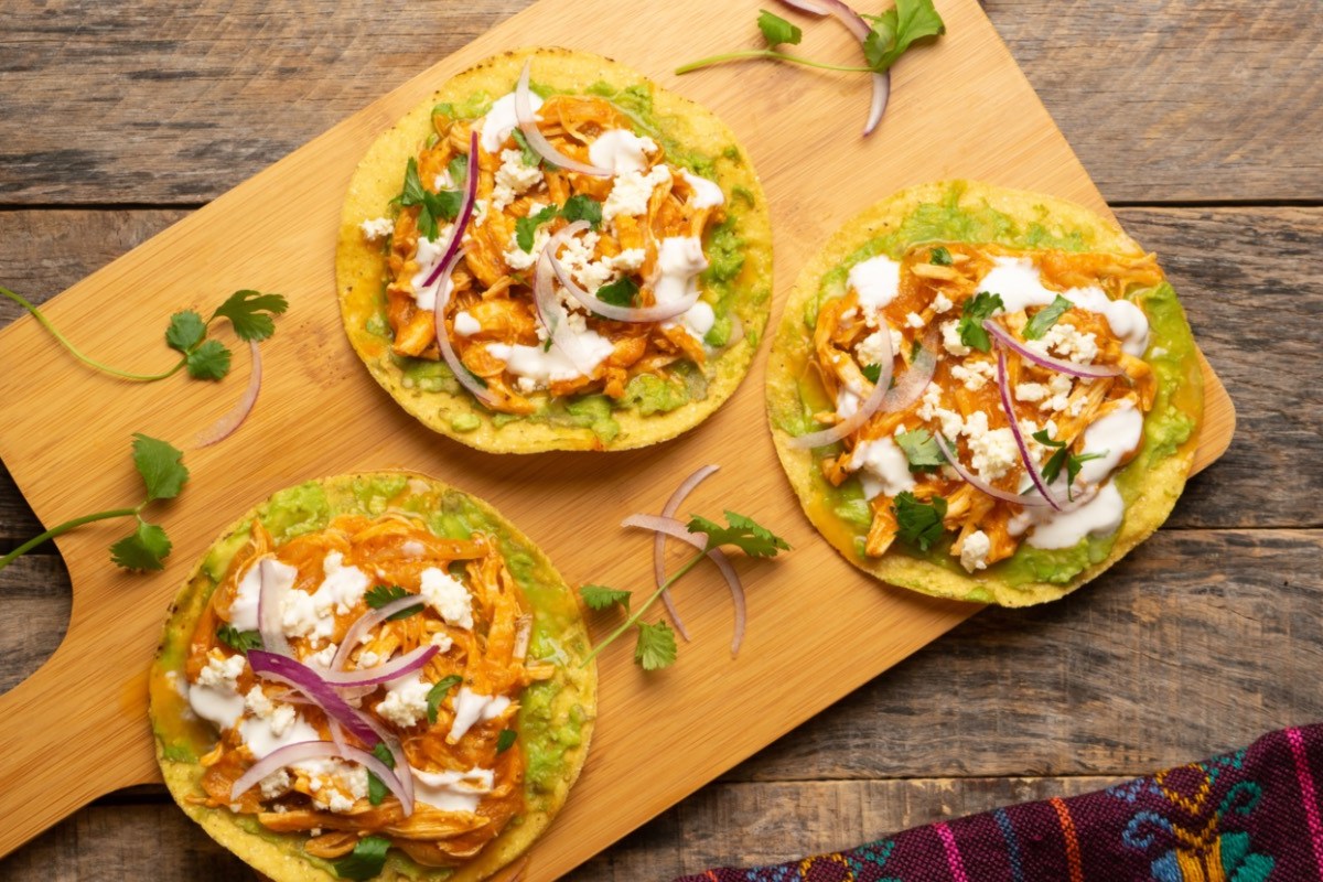 Drei Chicken Tinga Tostadas auf einem Holzbrett in der Draufsicht.