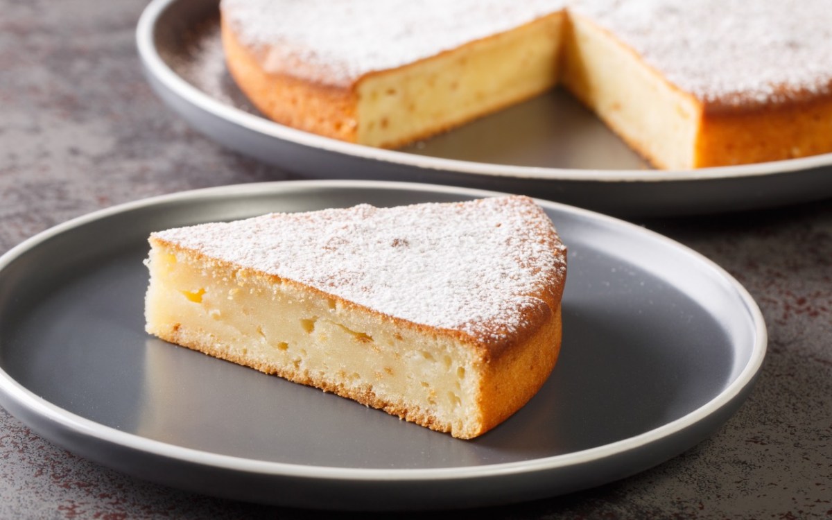 Ein Stück Joghurtkuchen mit 3 Zutaten auf einem Teller. Im Hintergrund der restliche Kuchen.