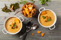 Zwei Schüsseln mit Pfifferlingcremesuppe und einer Schale Pfifferlingen.