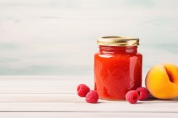 Ein Glas Pfirsich-Melba-Marmelade mit Himbeeren und Pfirsich daneben