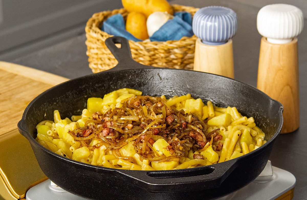 Älplermagronen mit Röstzwiebeln in einer gusseisernen Pfanne.