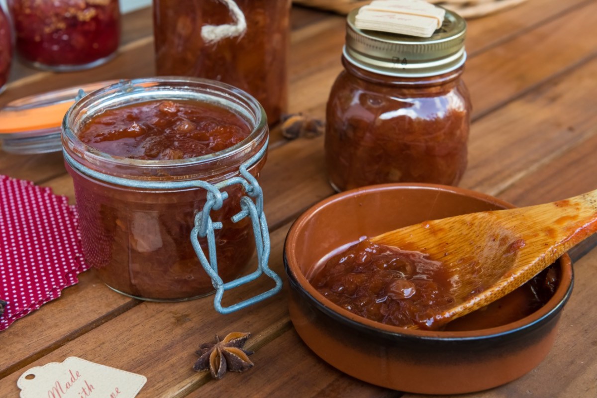 Mehrere Gläser Zwetschgen-Chitney. Daneben ein Holzlöffel mit Chutney, der in einer kleinen Schale liegt.