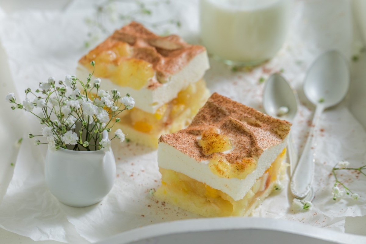 Zwei Stücke Apfel-Zimt-Torte auf einem Serviertablett. Daneben sind eine Vase mit Blumen und ein Löffel.