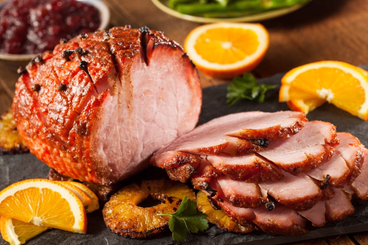 Ein Honey Glazed Ham mit karamellisierten Ananasscheiben, der zur Hälfte in Scheiben geschnitten wurde.