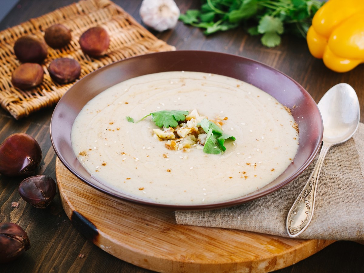 Ein Teller Maronensuppe mit Bergkäse, daneben ein Löffel und Maronen.