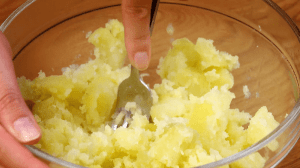 Gekochte Kartoffeln werden in Schüssel mit Gabel zerdrückt