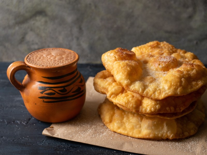 Buñuelos: mexikanische Weihnachtskrapfen neben einer Tasse mexikanischer heißer Schokolade.