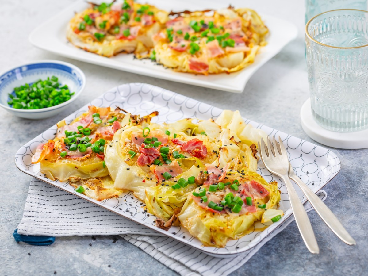 Zwei Servierplatten mit gebackenem Weißkohl mit Parmesan und Speck auf einem Tisch