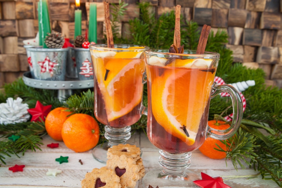 2 Glastassen mit Orangenpunsch. Der Hintergrund ist weihnachtlich dekoriert.