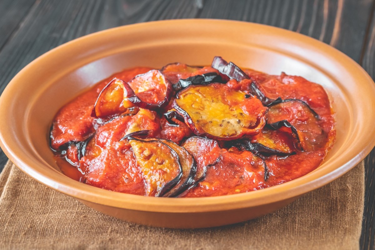 Eine Portion gebratene Aubergine in Tomatensoße in einem tiefen Teller.