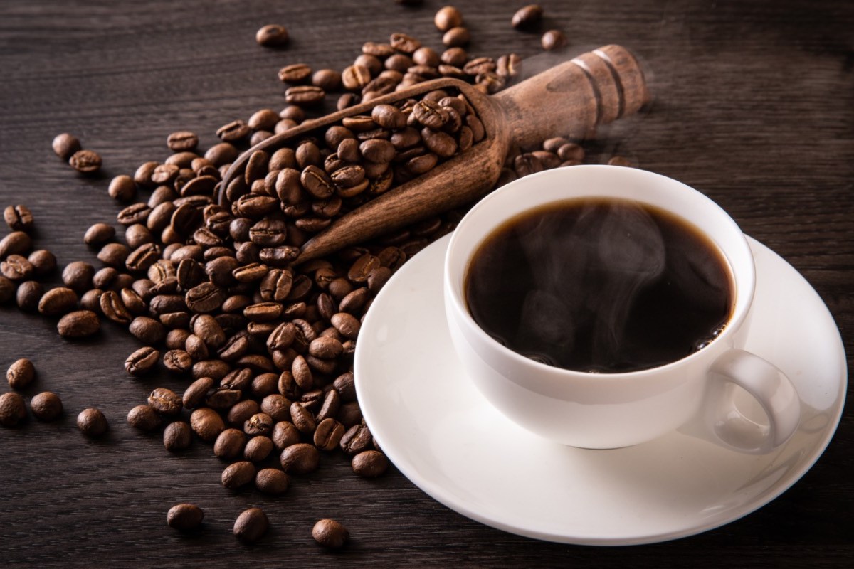 Wie wird Kaffee entkoffeiniert: Eine Tasse Kaffee neben der Kaffeebohnen liegen.