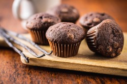 Ein paar Quark-Kakao-Muffins mit Schokolade auf einem Brett, daneben Vanilleschoten.