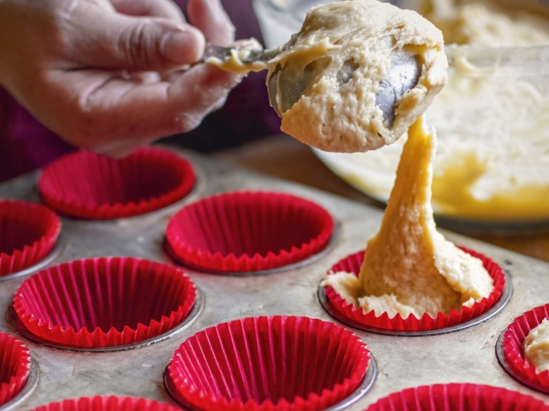Backen mit Silikonformen: Jemand füllt Teig in eine Silikon-Muffinform.