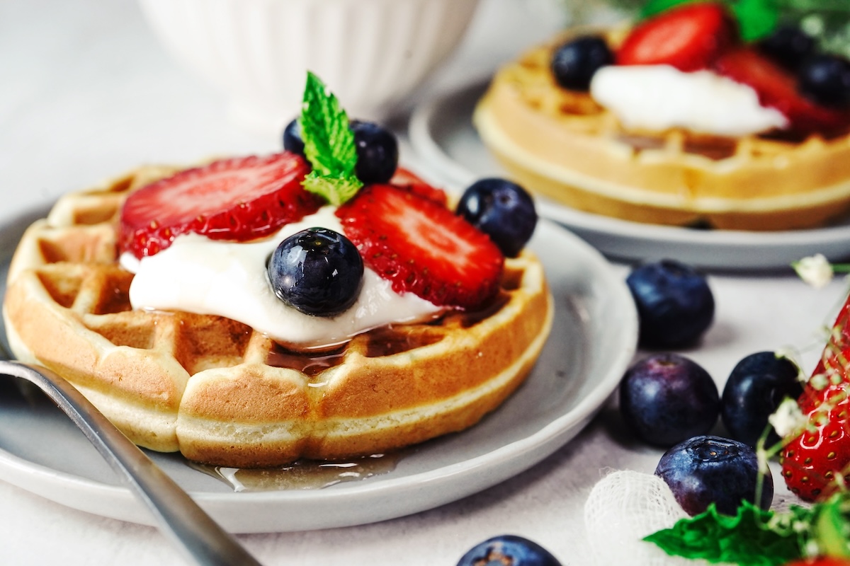 2 Teller mit je einer Frischkäse-Waffel getoppt mit Schmand, Beeren und Ahornsirup.