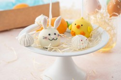 Osterhasen-Cake-Pop und ein Küken-Cake-Pop auf einer Tortenplatte mit weiterer Deko.