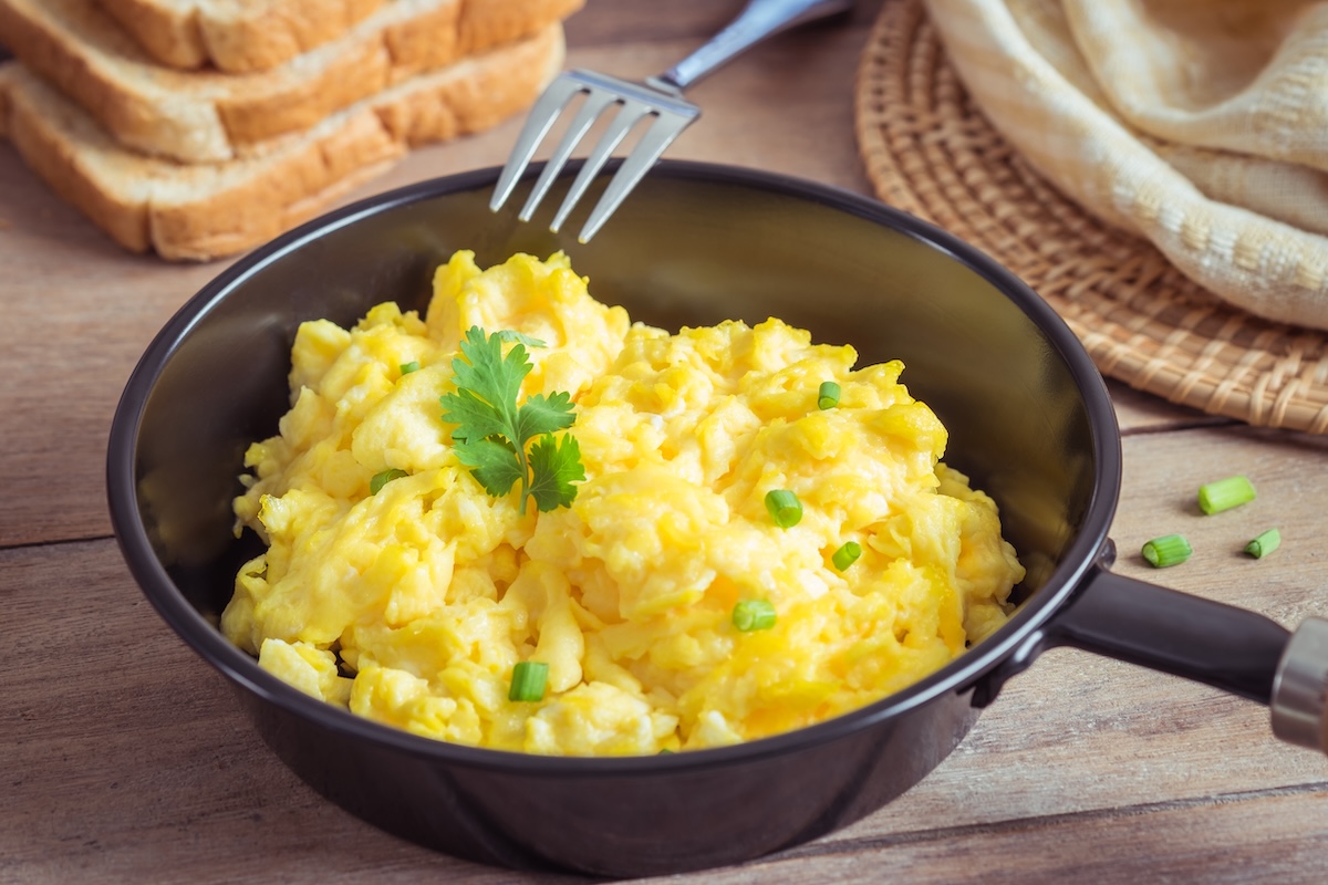 Rührei mit Hüttenkäse und Schnittlauch in einer kleinen Pfanne, daneben eine Gabel und Toastbrotscheiben.