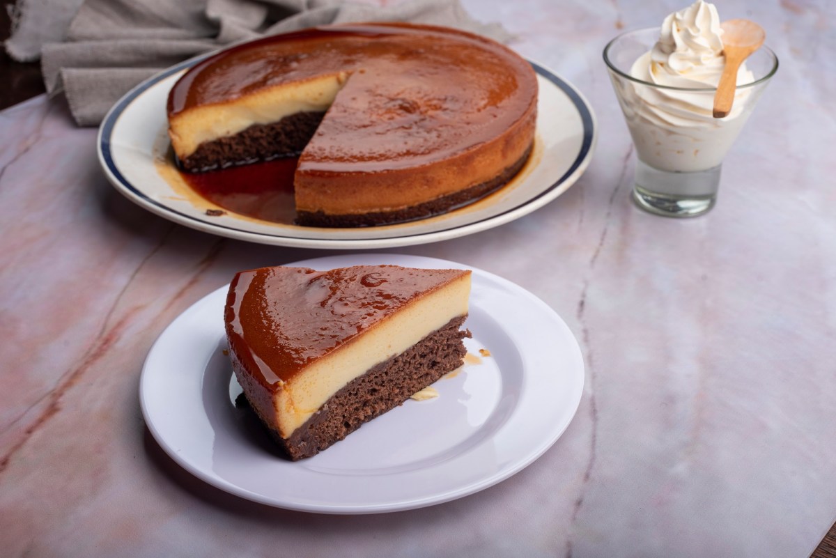 Ein Stück Schoko-Flan-Kuchen auf einem Teller. Im Hintergrund steht der restliche Kuchen.