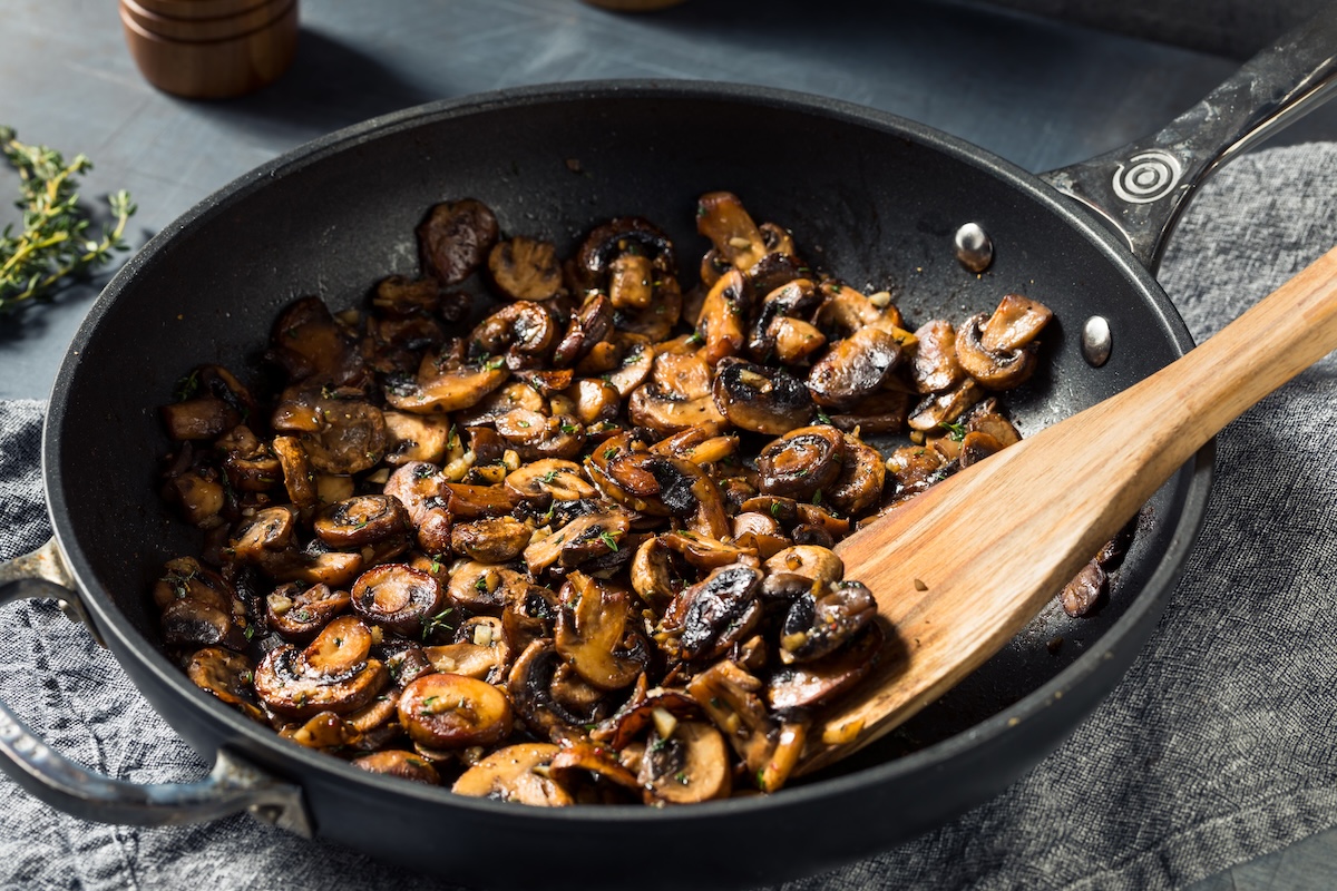 Champignons mit Kräuter-Chili-Soße in einer Pfanne mit einem Holzlöffel. Nahaufnahme.
