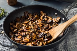 Champignons mit Kräuter-Chili-Soße in einer Pfanne mit einem Holzlöffel. Nahaufnahme.