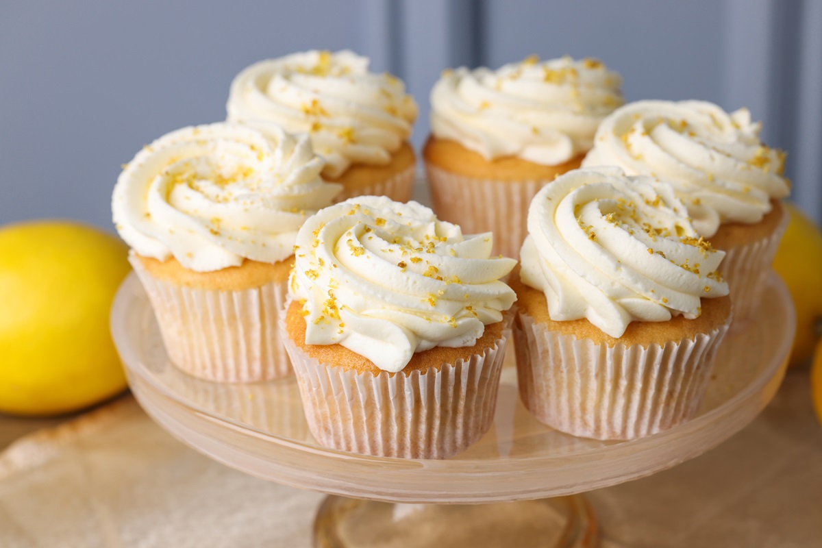 Eierlikör-Cupcakes auf einem Tortenständer. Im Hintergrund liegt eine Zitrone.