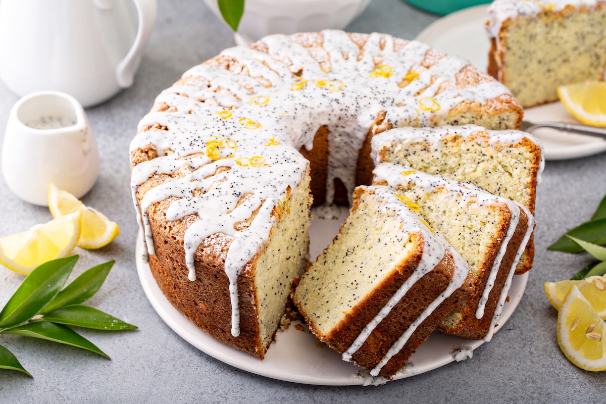 Ein angeschnittener Eierlikör-Gugelhupf mit Mohn und Zuckerguss, daneben ein paar Zitronenscheiben und Kännchen.