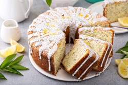 Ein angeschnittener Eierlikör-Gugelhupf mit Mohn und Zuckerguss, daneben ein paar Zitronenscheiben und Kännchen.