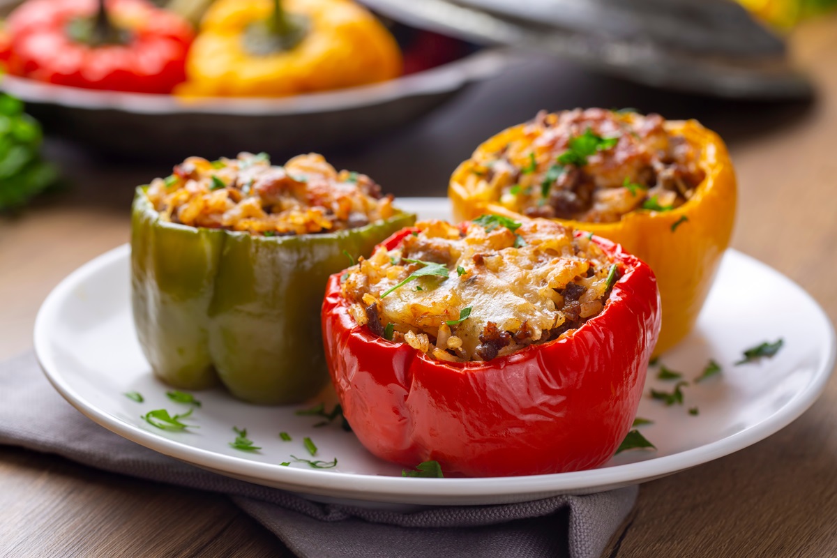 Drei Mal gefüllte Paprika mit Reis und Hackfleisch auf einem weißen Teller.