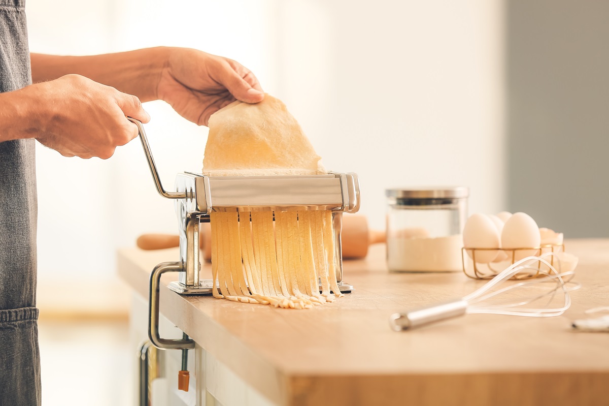 Eine Person dreht italienischen Nudelteig durch eine Nudelmaschine.