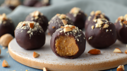 Mehrere Kichererbsen-Energyballs liegen auf einem runden Brett. Die vorderste Kugel ist aufgeschnitten und gibt den Blick auf die Füllung frei.