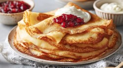 Ein Stapel Svele, norwegische Pfannkuchen, auf einem Teller. Dazu werden Preiselbeerkompott und Schmand serviert.