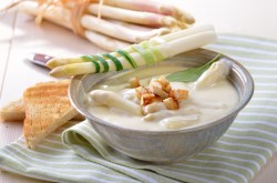 vegane Spargelcremesuppe in einer Schüssel, garniert mit Spargelspitzen und Crôutons. Daneben Toastbrotscheiben und Spargelstangen.