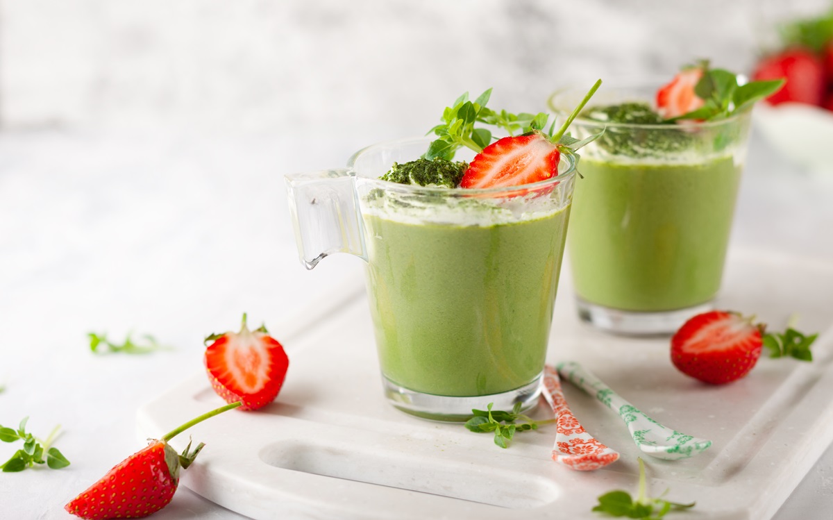 Zwei Gläser mit Waldmeister-Mousse, garniert mit frischen Erdbeeren.