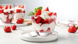 Erdbeer-Mascarpone-Schichtdessert im Glas, im Hintergrund weitere Gläser mit dem Nachtisch sowie frische Erdbeeren.