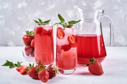 2 Gläser Erdbeerlimonade mit Mango und Banane, daneben ein Krug mit der Limo und einige frische Erdbeeren.