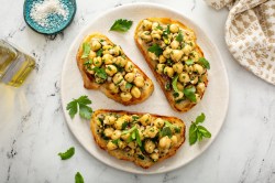 Drei Scheiben Kichererbsen-Bruschetta auf einem hellen Teller.