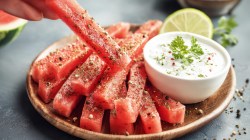 Wassermelonen-Pommes mit Dip auf einem Teller. Jemand nimmt sich eine Pommes.