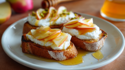 Drei Burrata-Toasts mit Apfel und Honig liegen auf einem Teller.