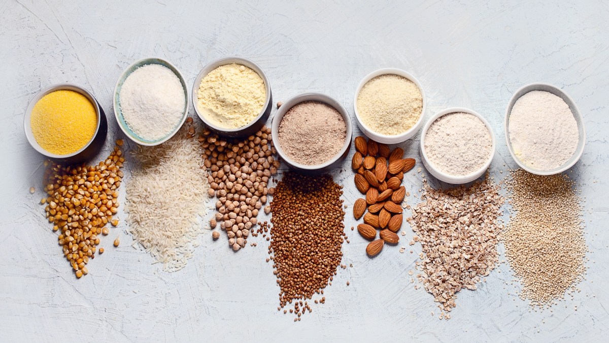 Draufsicht: Verschiedene Schalen mit unterschiedlichen Mehlsorten ohne Gluten. Vor der Schale liegt das jeweilige Korn, der Samen, etc. verstreut.