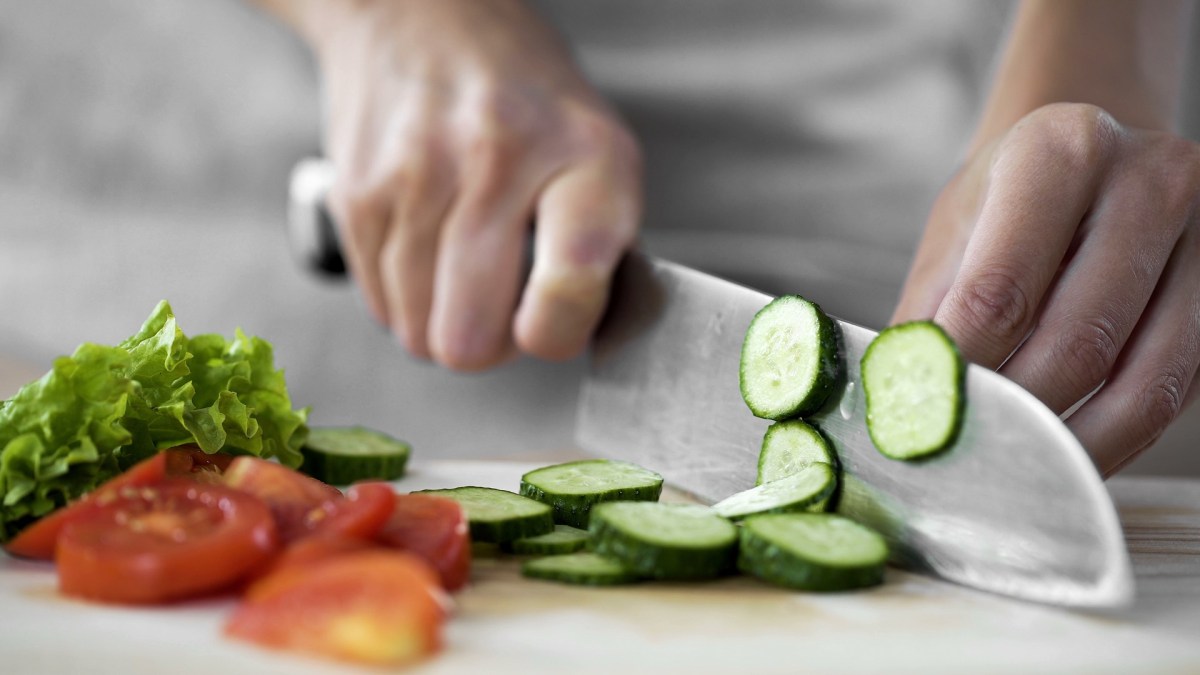 ZWILLING selbstschärfender Messerblock: Ein Ausschnitt, auf dem jemand ein Messer in der Hand hält und Gurke damit schneidet. Auf dem Brett liegen Gurkenscheiben, Tomatenscheiben und Salat. Der Hintergrund ist verschwommen.
